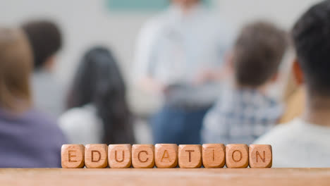 Education-Concept-With-Wooden-Letter-Cubes-Or-Dice-Spelling-Education-With-Student-Lecture-In-Background